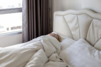 A mature man sleeps alone on a bed in summer covered with a white blanket. Sound sleep and comfortable res